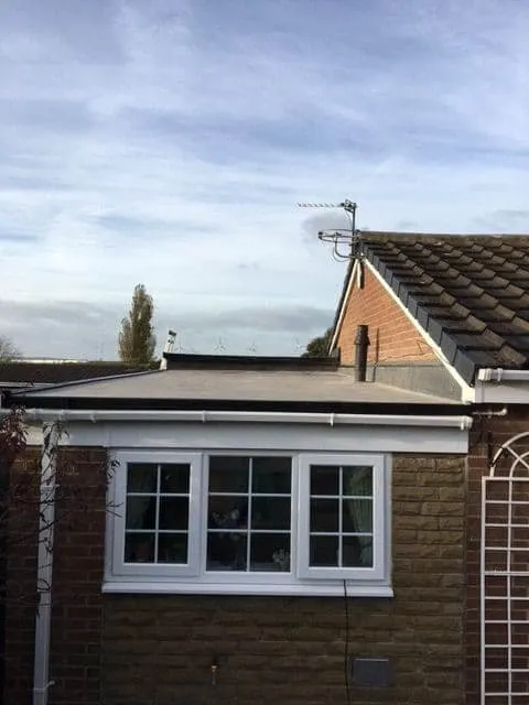 A completed dark flat roof over a single-storey part of a house in Consett, with white fascia and guttering, and the pitched main roof behind.