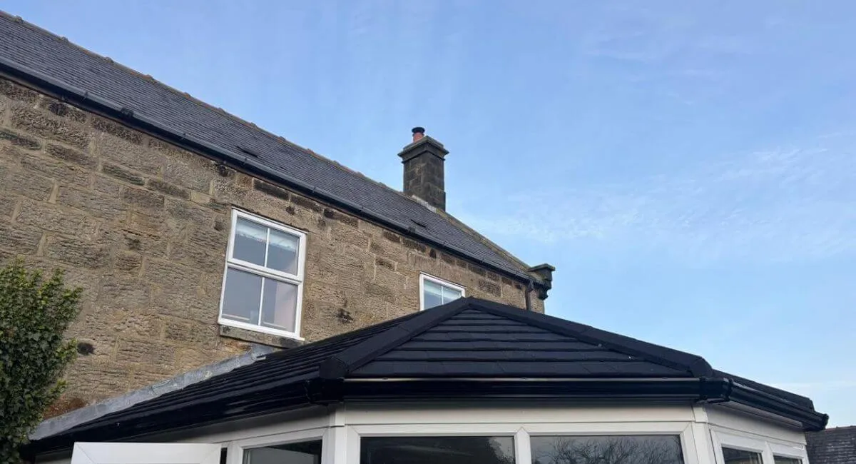 A stone-built property in Hexham, Northumberland with a completed dark tiled conservatory roof, seen from the garden under a clear sky.