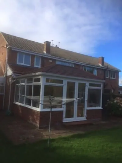 A white conservatory with a tiled roof and glazed double doors at the back of a brick house in Houghton-le-Spring, with a rotary washing line on the lawn.