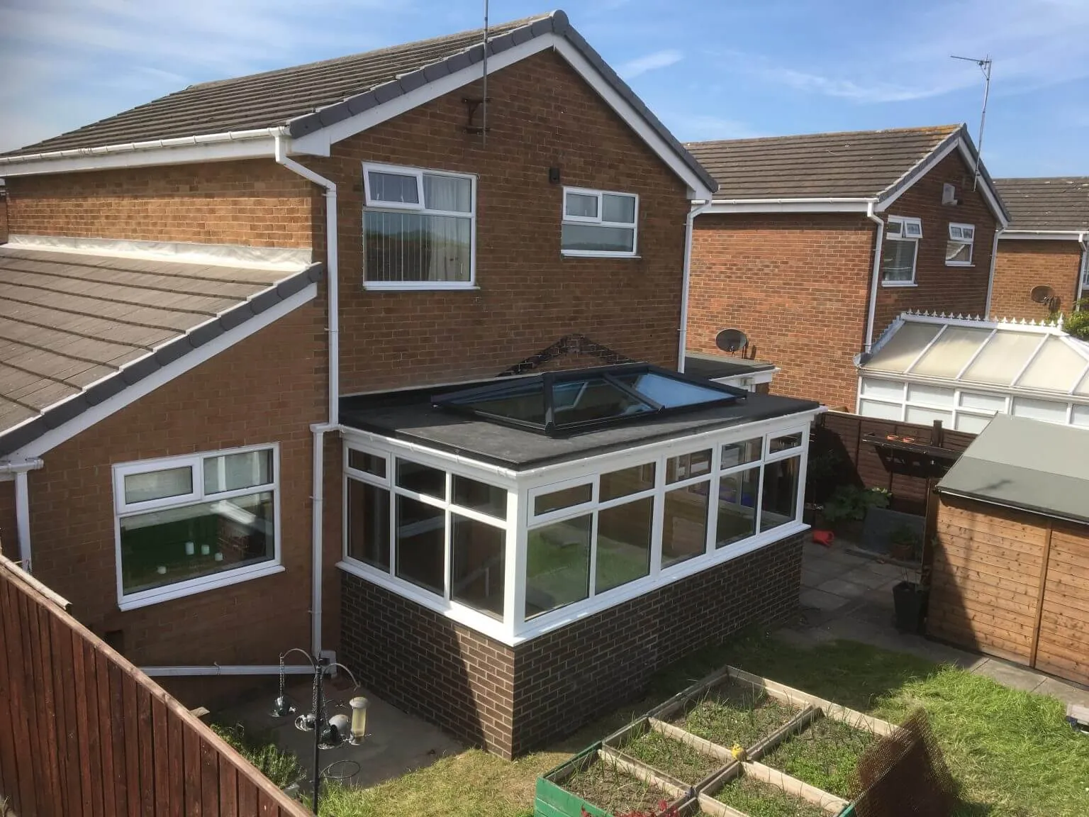 A black-framed glazed roof lantern fitted into the flat roof of an existing white-framed conservatory at a house in Otterburn, Northumberland.
