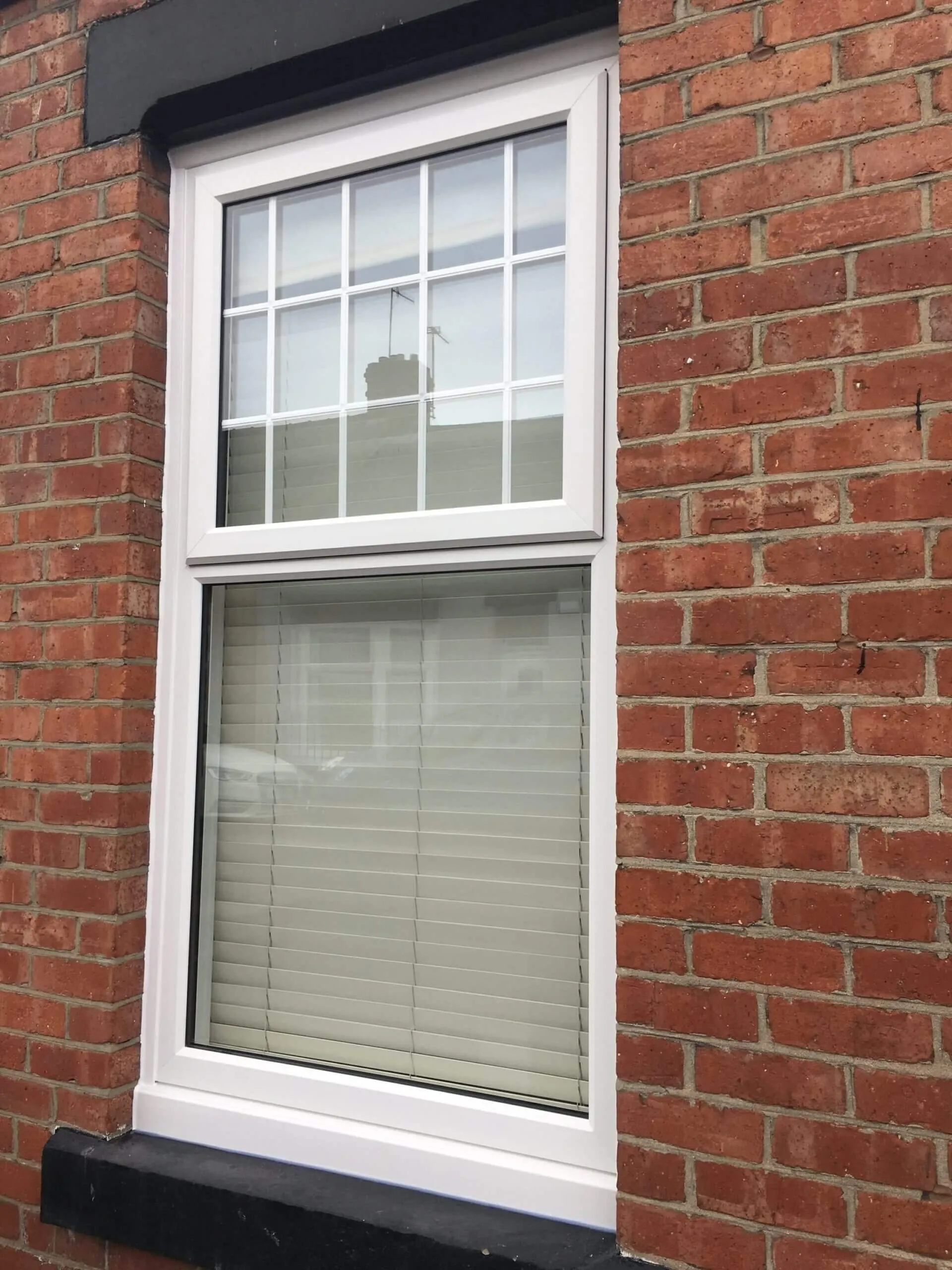A white-framed window in a red-brick house wall in Redcar, with glazing bars across the upper opening light and a blind behind the lower pane.