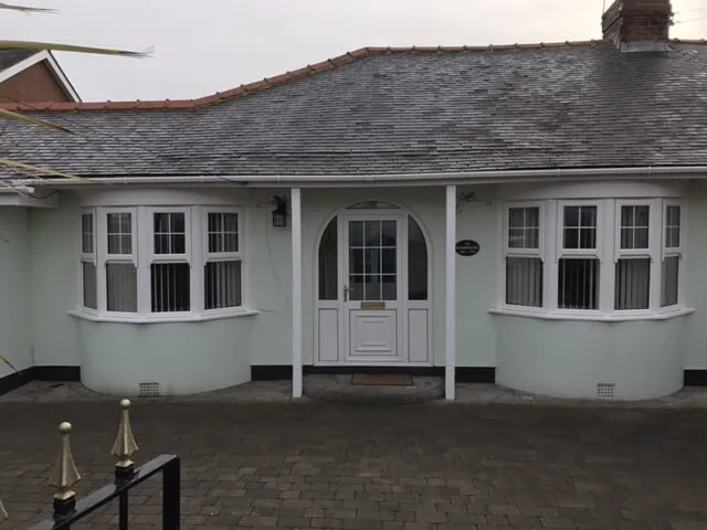 A pale rendered bungalow in Saltburn with two white projecting bay windows, with glazing bars to the upper lights, either side of a central arched front door.