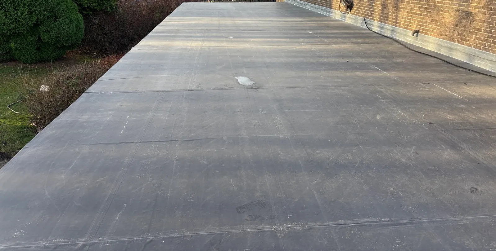 A completed EPDM flat roof in Tanfield Lea, with welded seams running across the membrane and a brick parapet with metal coping along one edge.