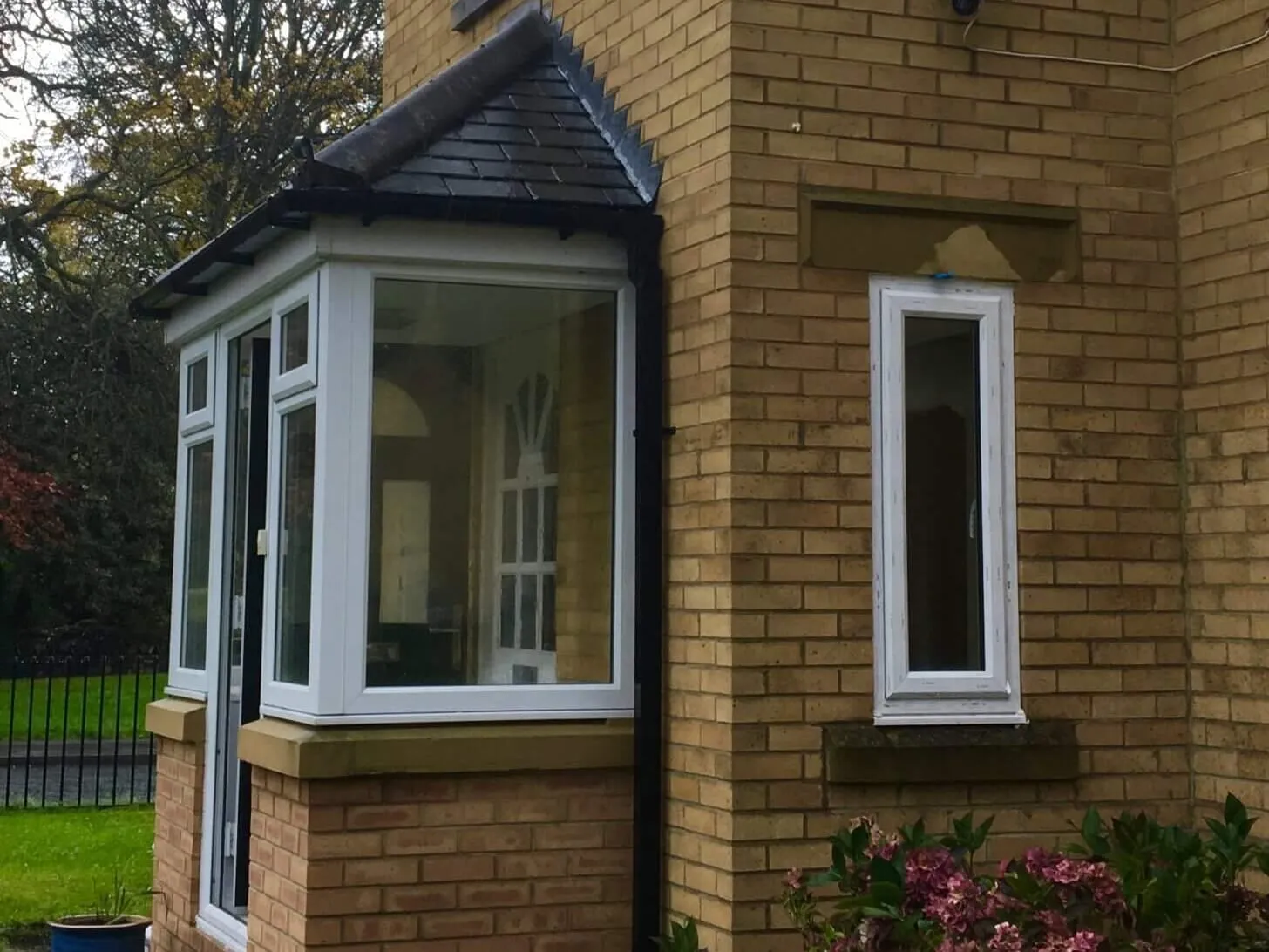 A white-framed porch with angled glazed sides at a house in Usworth, with a tall white-framed window in the buff-brick wall beside it.